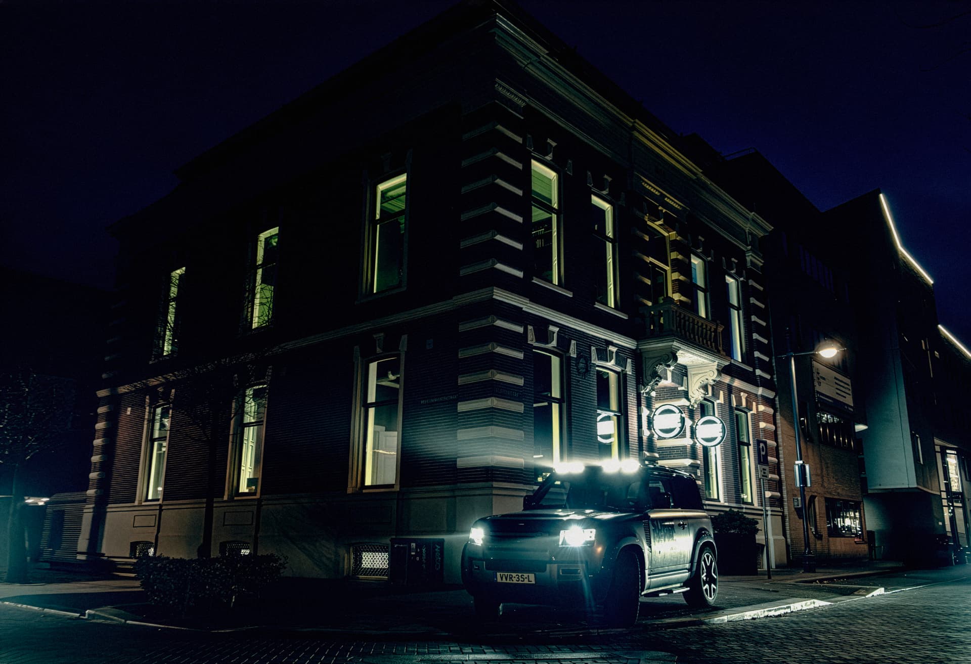 Hotel SuperRebel in Breda at night, a Land Rover Defender parked in front of the lit facade